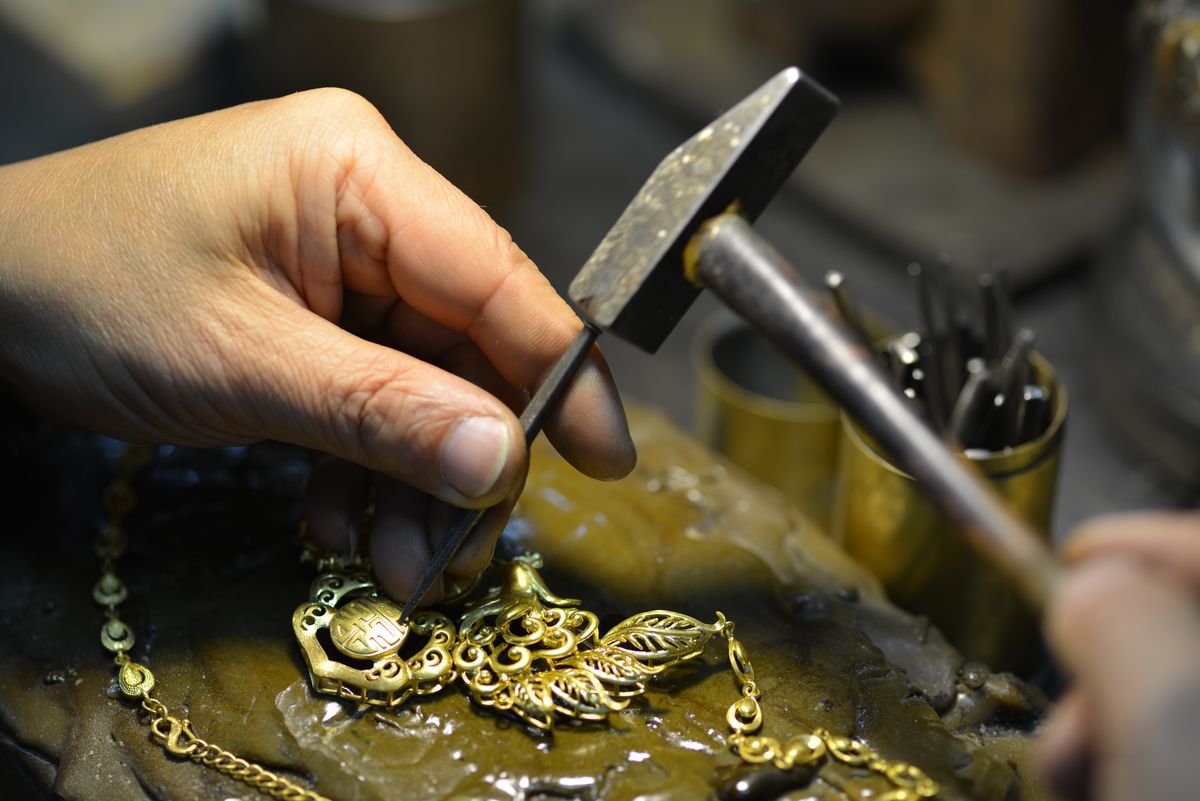 Een hand met hamer en drevel werkt een gouden hanger af op de werkbank