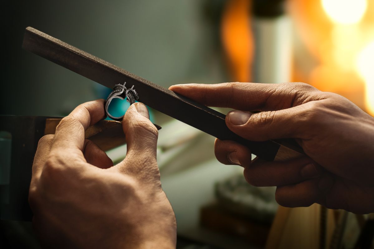 Twee handen werken een ring in wording af met een vijl aan de werkbank