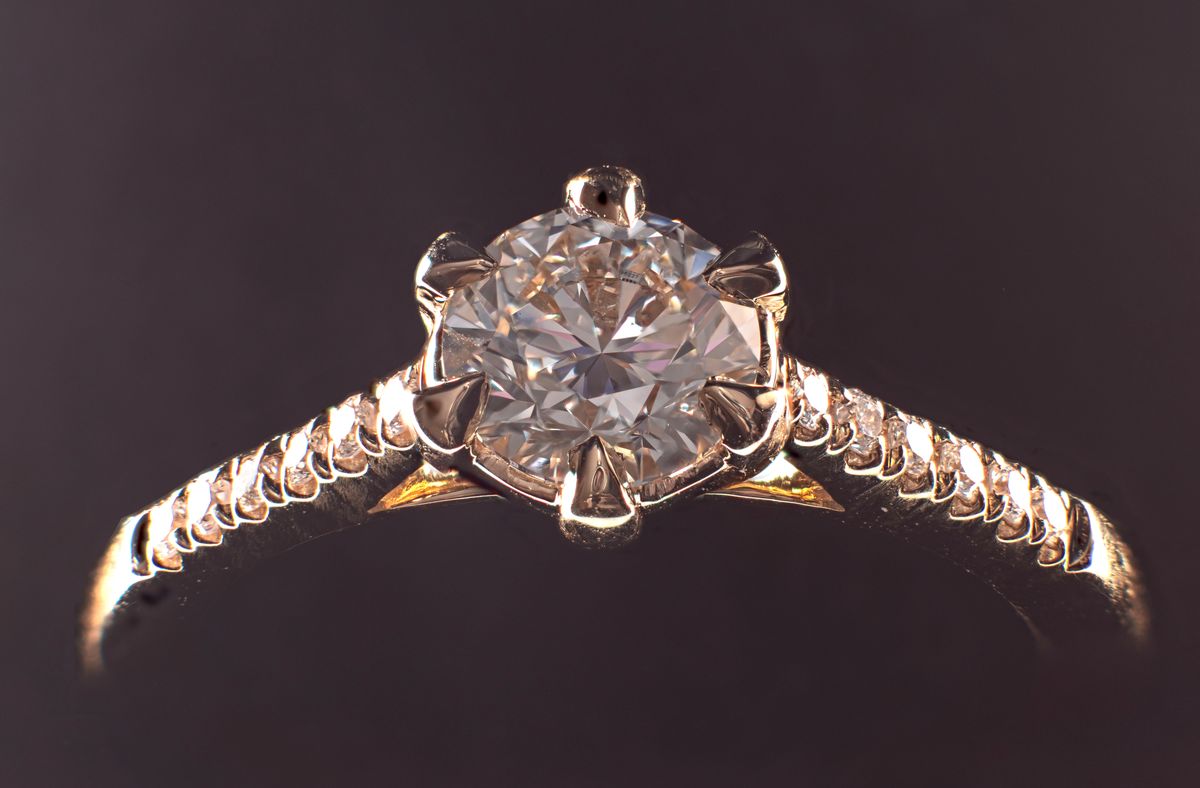 Verlovingsring met een ronde diamant in een zeskrappige zetting en kleine stenen in de band