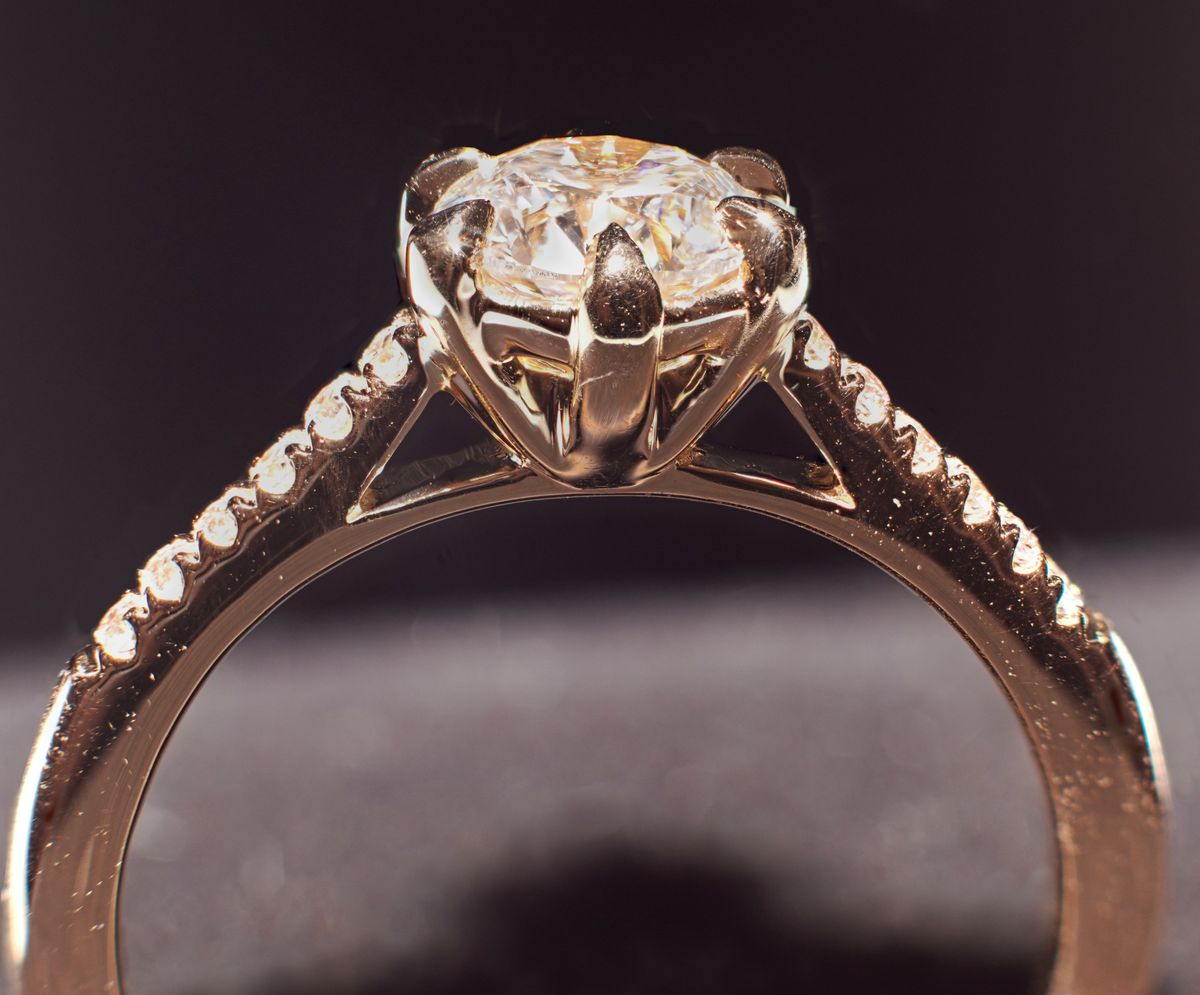 Zijaanzicht van een verlovingsring met een ronde diamant en kleine stenen in de band